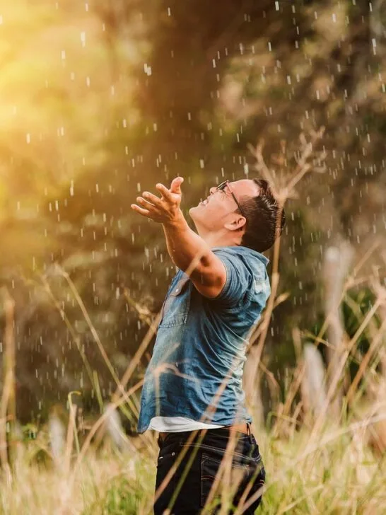 A man holding his arms out while standing in the rain in a field. Just one of the many ways to bring spontaneity into your daily routine