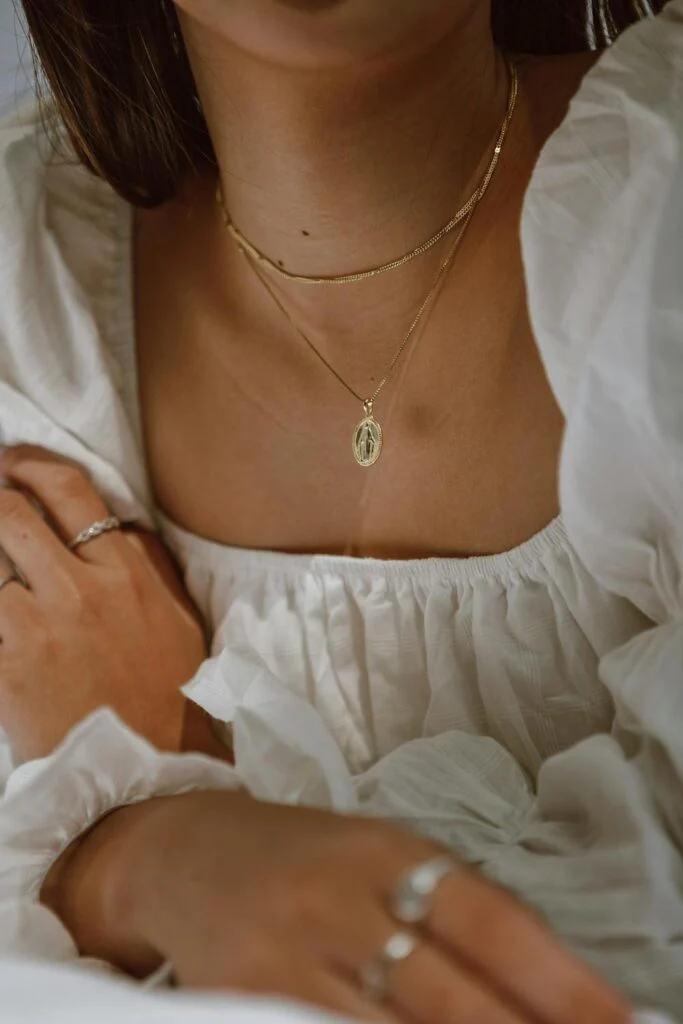 Close up image of two necklaces a woman is wearing with a white blouse