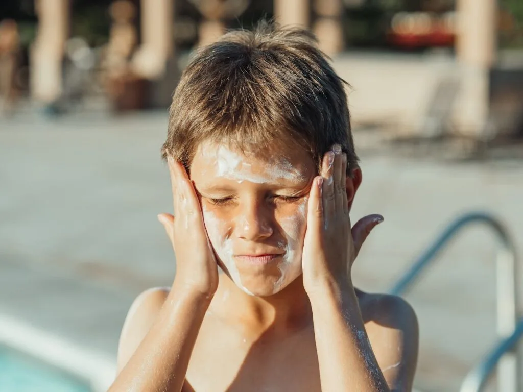 A child applying sunscreen to his face after learning how to choose the best sunscreen for your skin type
