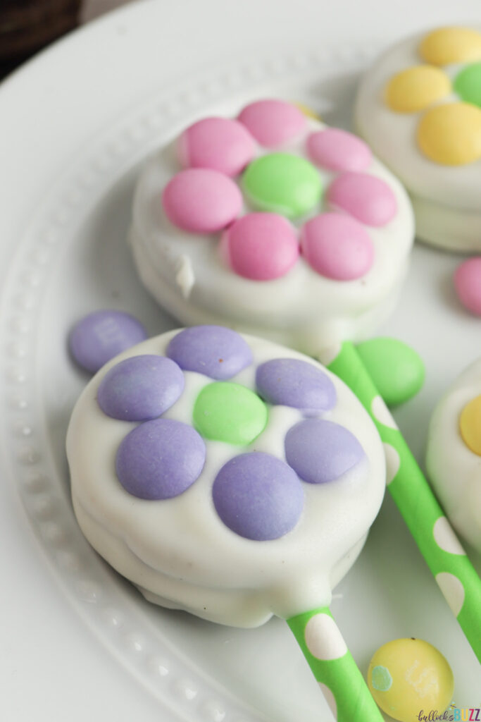 A close up picture of a finished Oreo Flower Pop made with purple M&Ms around a green M&M in the center of the cookie