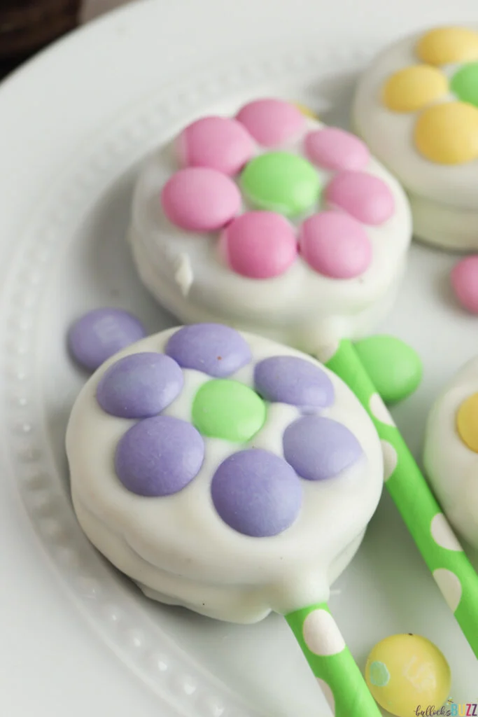 A close up picture of a finished Oreo Flower Pop made with purple M&Ms around a green M&M in the center of the cookie