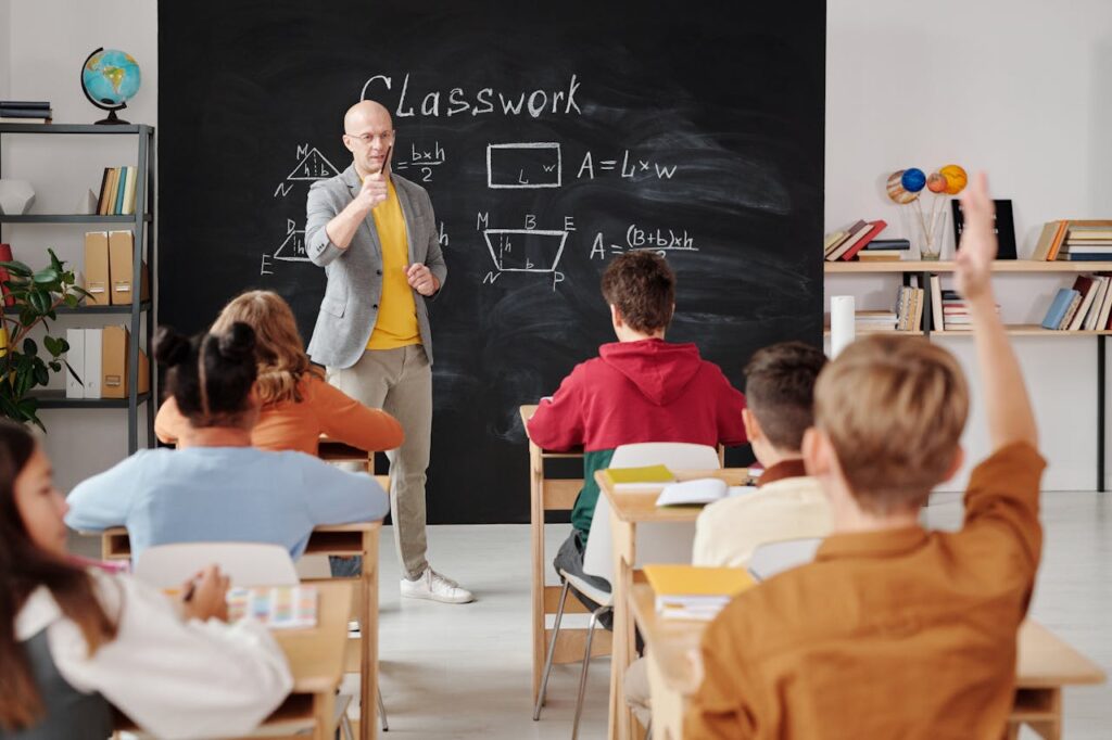Kids in class facing a blackboard with one raising his hand. Multivitamins for growing children also help with mental and intellectual development,