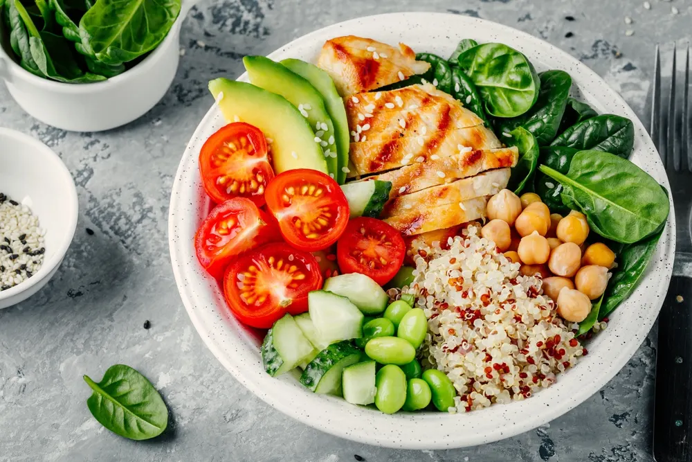Buddha bowl with spinach salad, quinoa, chickpeas, grilled chicken, avocado, tomatoes, cucumbers, sesame seeds. — Stock Photo, Image