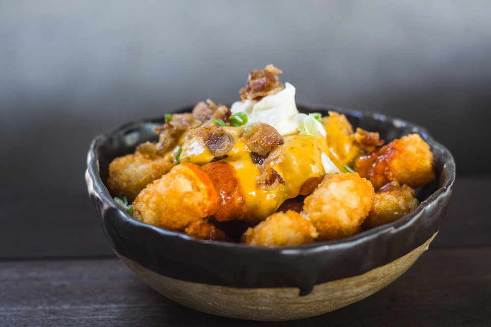 Crispy tater tots doused mercilessly in spicy jalapeno cheese sauce, maple-glazed bacon and sour cream. Finished with a splash of hot sauce — Stock Photo, Image