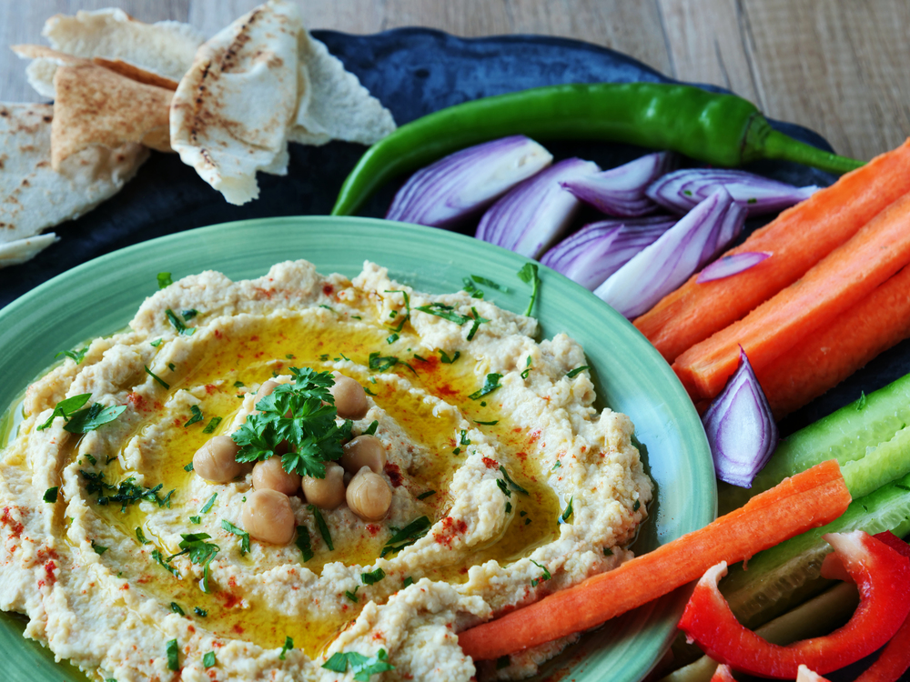 Hummus topped with whole chickpeas and olive oil served with vegetables — Stock Photo, Image