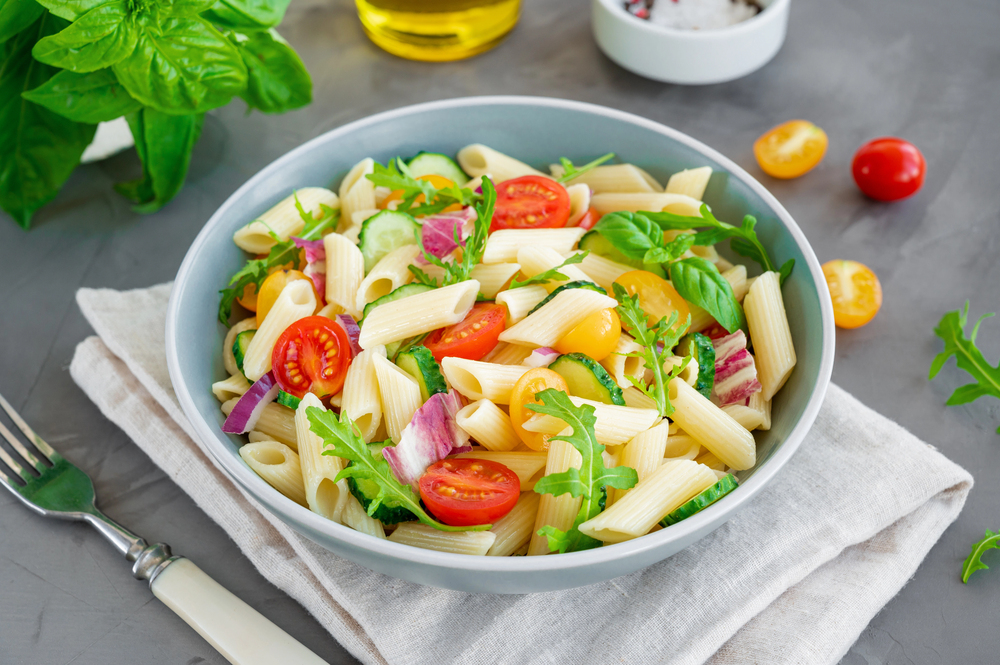 Healthy vegan pasta salad with tomatoes, cucumbers, red onions and arugula in a bowl on a dark gray background. Copy space — Photo