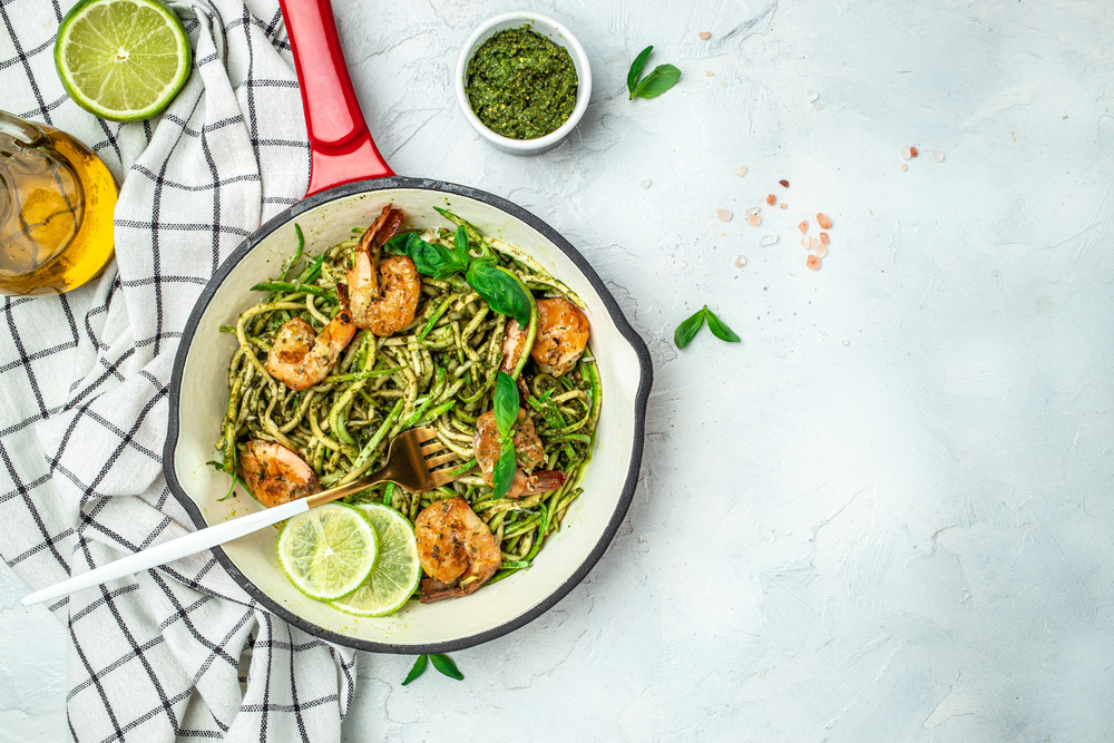 Zucchini spaghetti with pesto sauce and grilled shrimp skewers in pan. keto low carb diet. banner, menu, recipe place for text, top view.