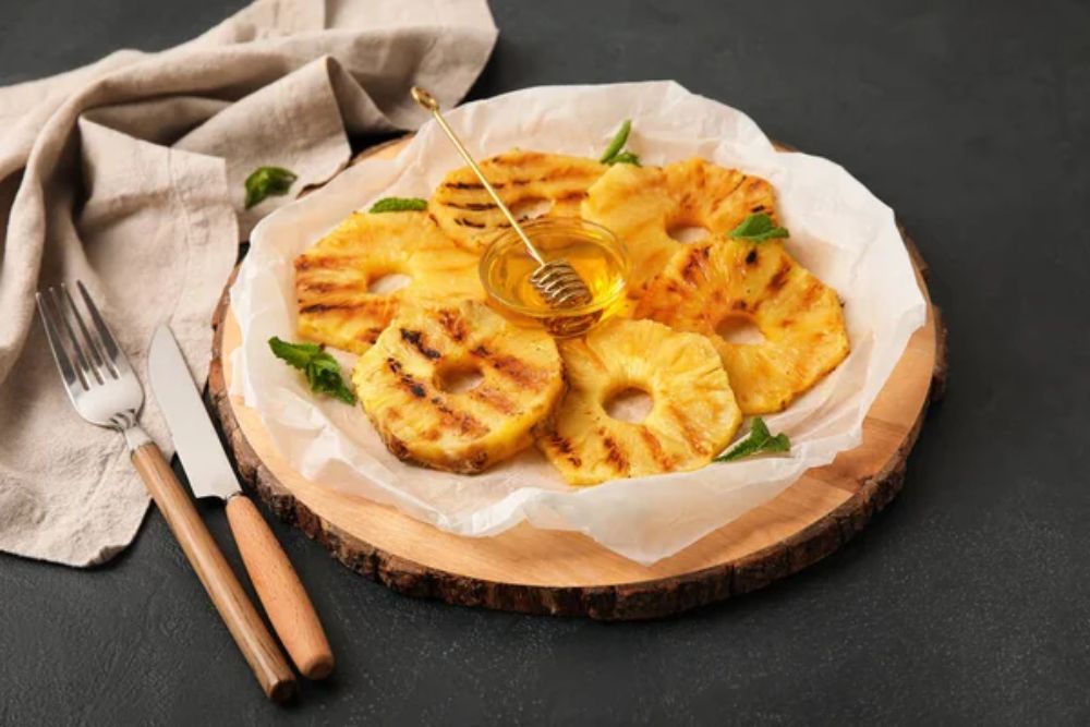 Board with grilled pineapple slices and honey