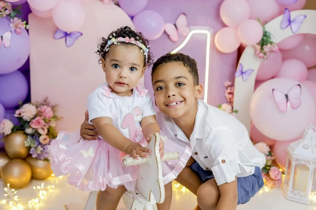 A brother and sister posing together in front of balloons for her birthday