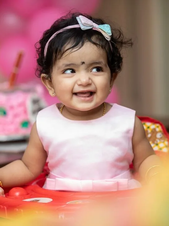 A little girl with a cake behind her posing for her birthday. Use these tips on ways to personalize your kid’s birthday party