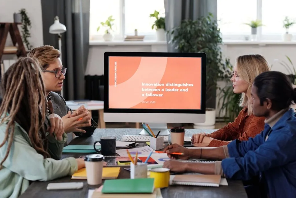 A group of people sitting around the table looking at a monitor using technology as part of their new employee onboarding process