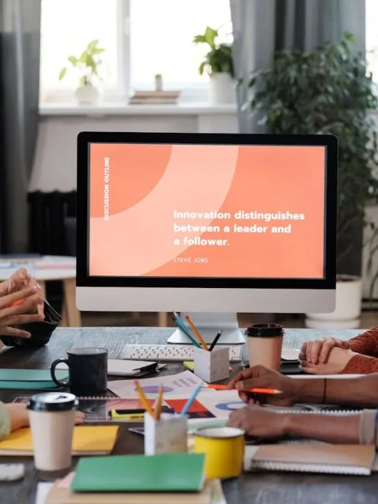 A group of people sitting around the table looking at a monitor using technology as part of their new employee onboarding process