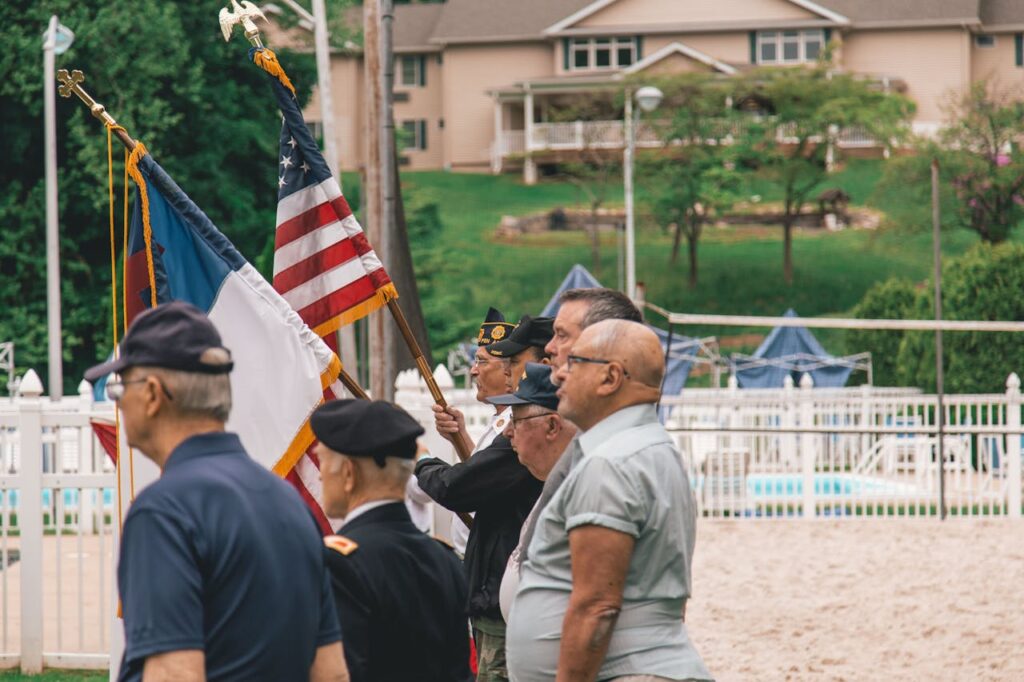 Group of veterans, both young and senior, standing together with one holding the U.S. flag and another holding another military flag, representing unity and support through senior veterans benefits.