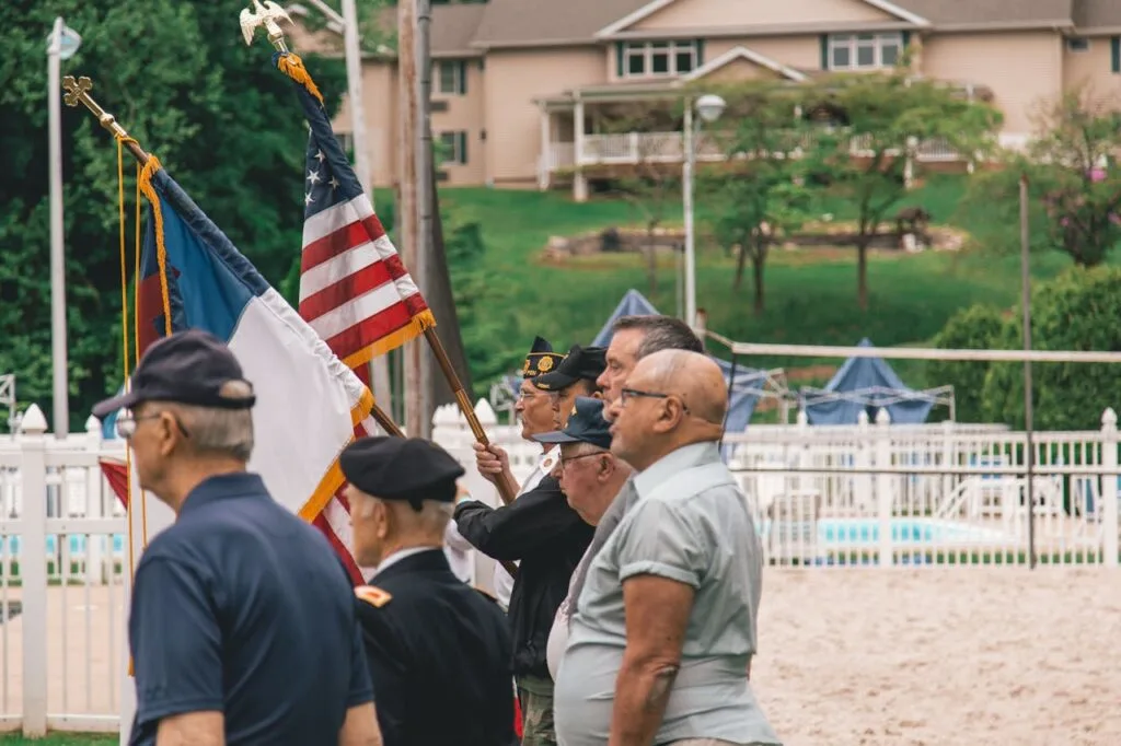 Group of veterans, both young and senior, standing together with one holding the U.S. flag and another holding another military flag, representing unity and support through senior veterans benefits.