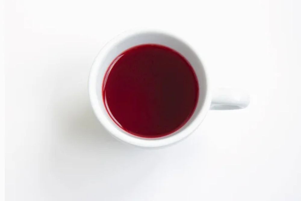 Red hibiscus tea in a white cup isolated on a white background.