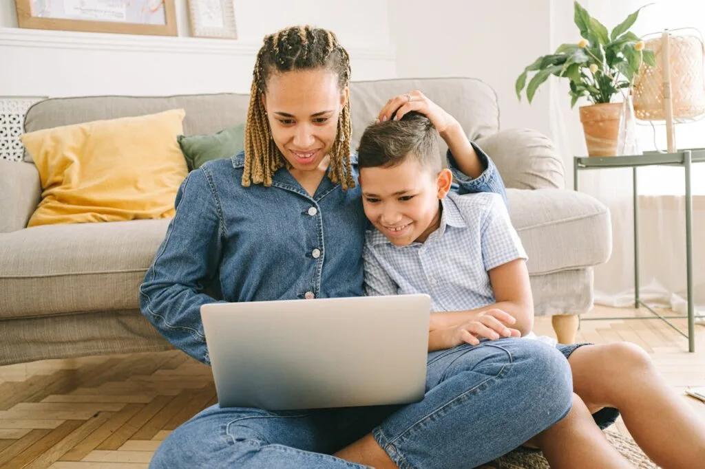A mom and son sitting on the floor playing digital card games together on her laptop