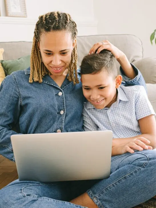 A mom and son sitting on the floor playing digital card games together on her laptop