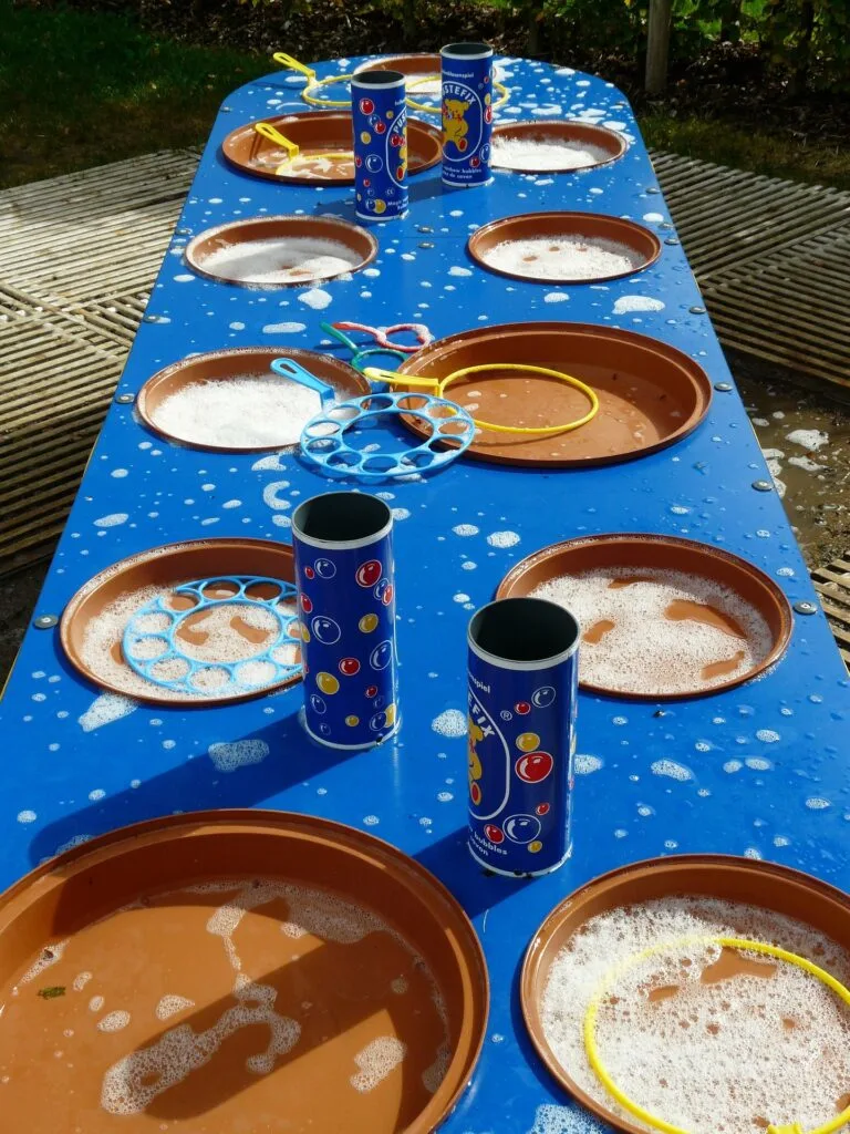 A table with trays of bubble mix and wands for kids to make bubbles with at a bubble themed summer party