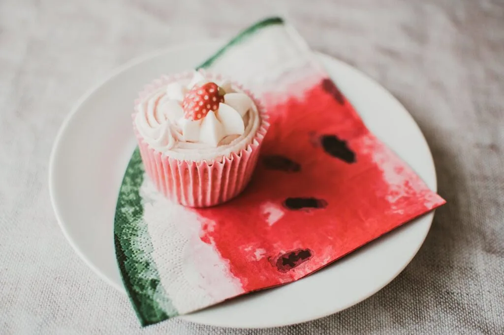 A cupcake on top of a watermelon-themed napkin sitting on a white plate
