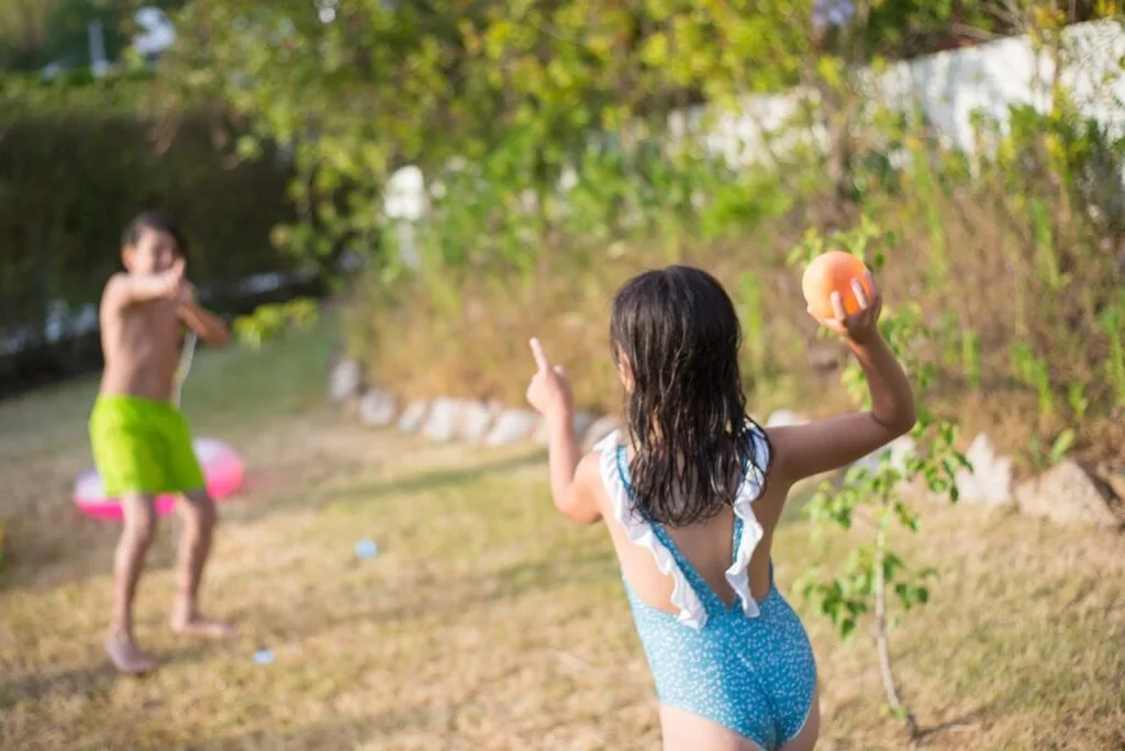 Two kids in swimsuits playing water balloon toss, one of the most fun outdoor games for summer parties