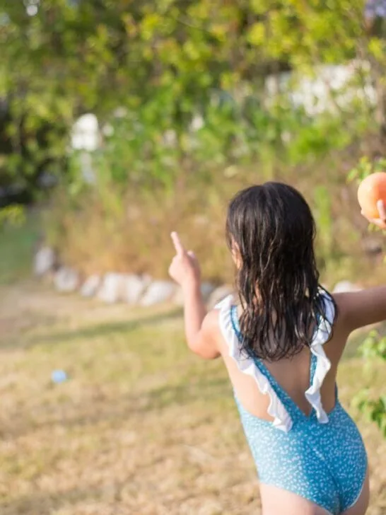 Two kids in swimsuits playing water balloon toss, one of the most fun outdoor games for summer parties