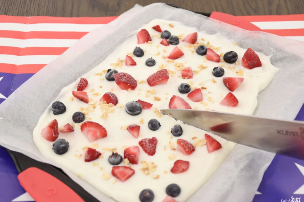 Using a knife to cut Frozen Yogurt Bark with blueberries, strawberries and granola for an easy no-bake summer recipe