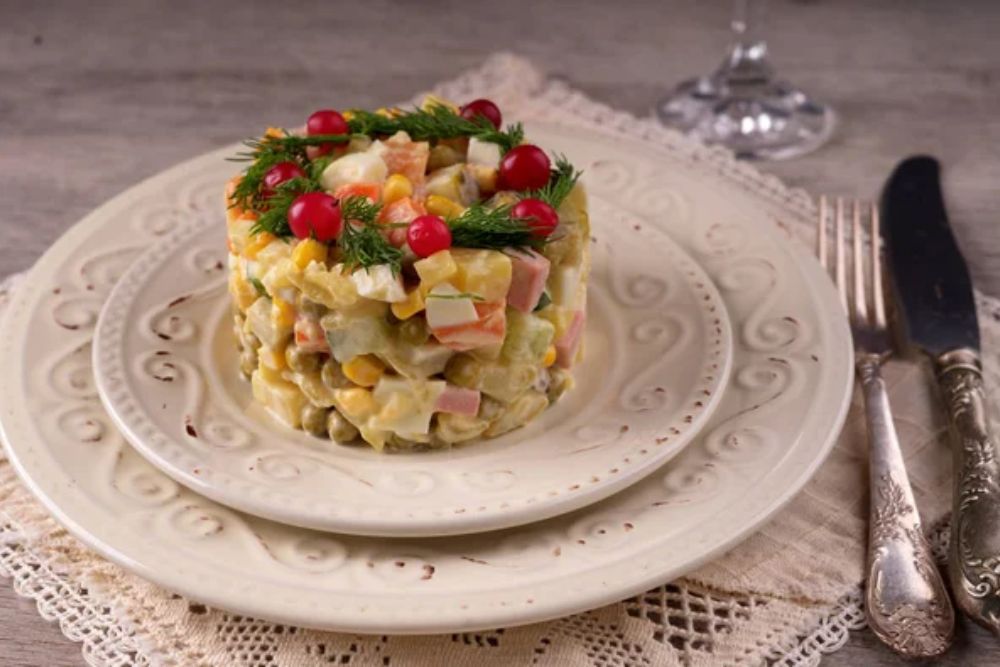 Russian salad on a white plate and cutlery on the table. — Photo