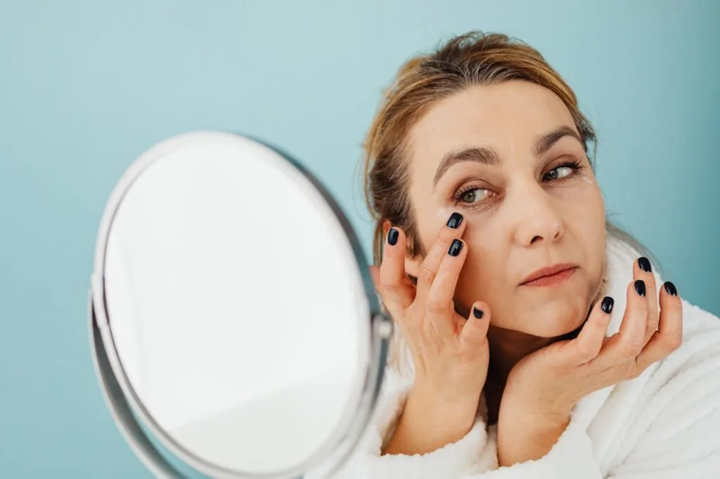 a woman looking in mirror applying moisturizer around her eyes as part of managing wrinkles after 40