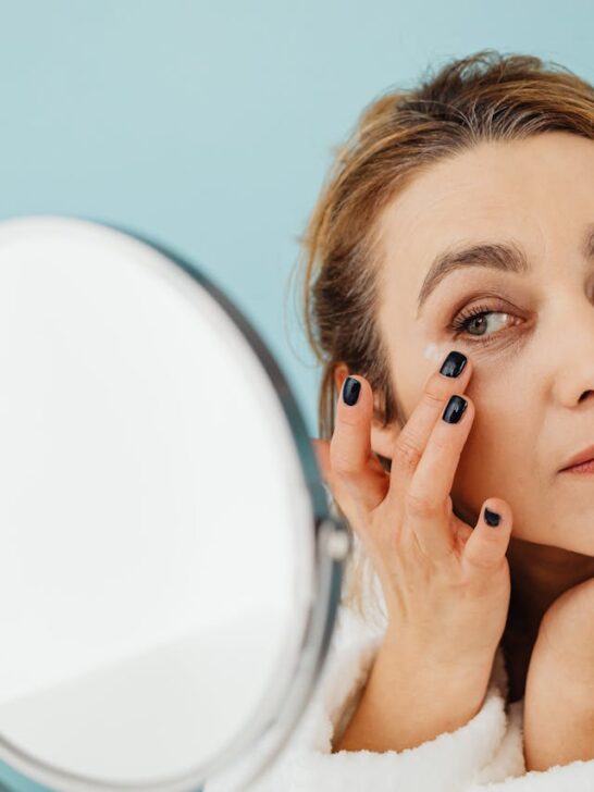 a woman looking in mirror applying moisturizer around her eyes as part of managing wrinkles after 40
