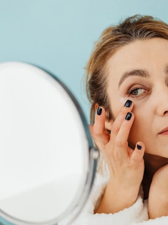 a woman looking in mirror applying moisturizer around her eyes as part of managing wrinkles after 40