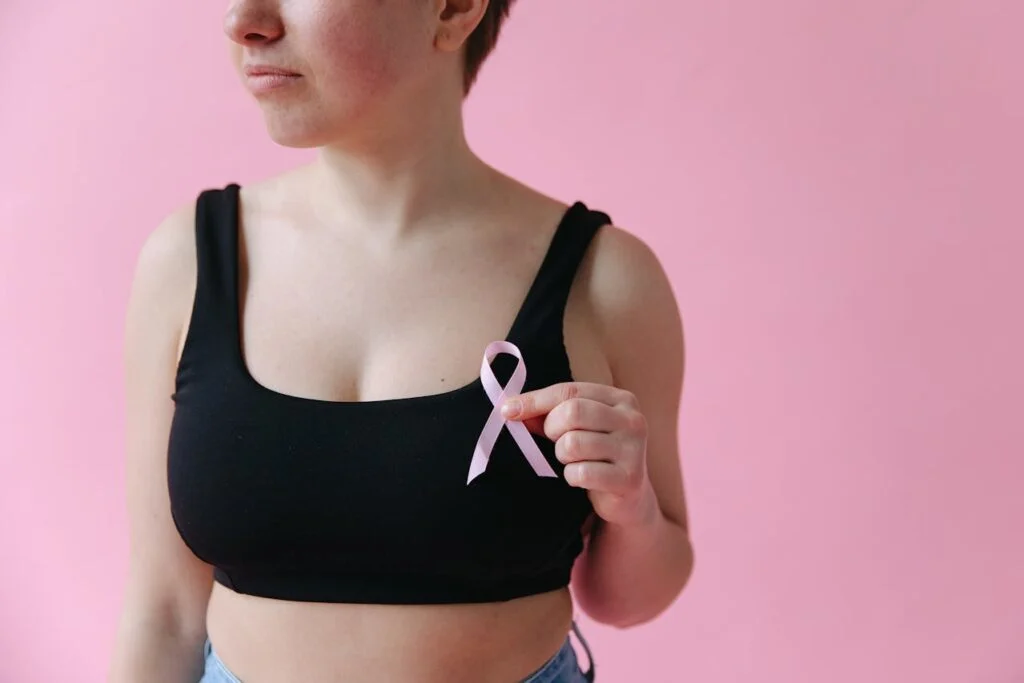 A woman in a black tank top holding a pink ribbon for breast cancer awareness