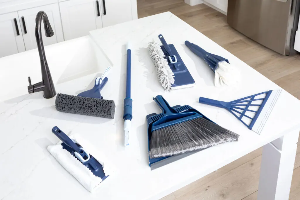 The full Casabella click clean and organize collection lying on a white counter next to a sink with a black faucet