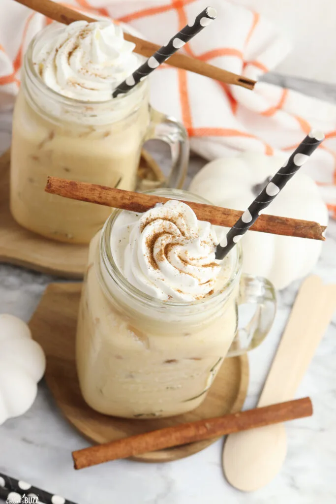 Overhead image of two glasses of Copycat Starbucks Pumpkin Cream Cold Brew om wood coasters and cinnamon sticks as an accent