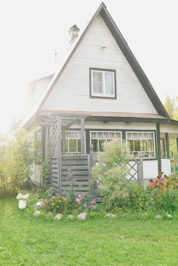 A white cottage with a steep angled roof and a pretty garden in front