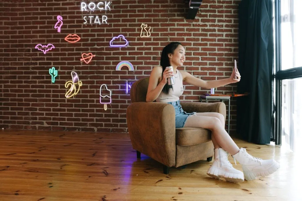 A girl sitting in her chair in front of a brick wall with several neon signs on it, showing how popular neon sign interior design is becoming.