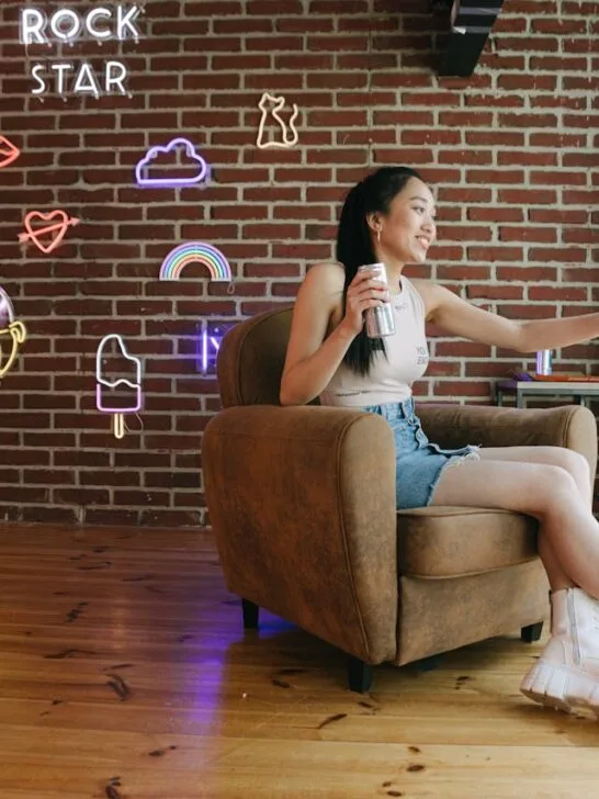 A girl sitting in her chair in front of a brick wall with several neon signs on it, showing how popular neon sign interior design is becoming.