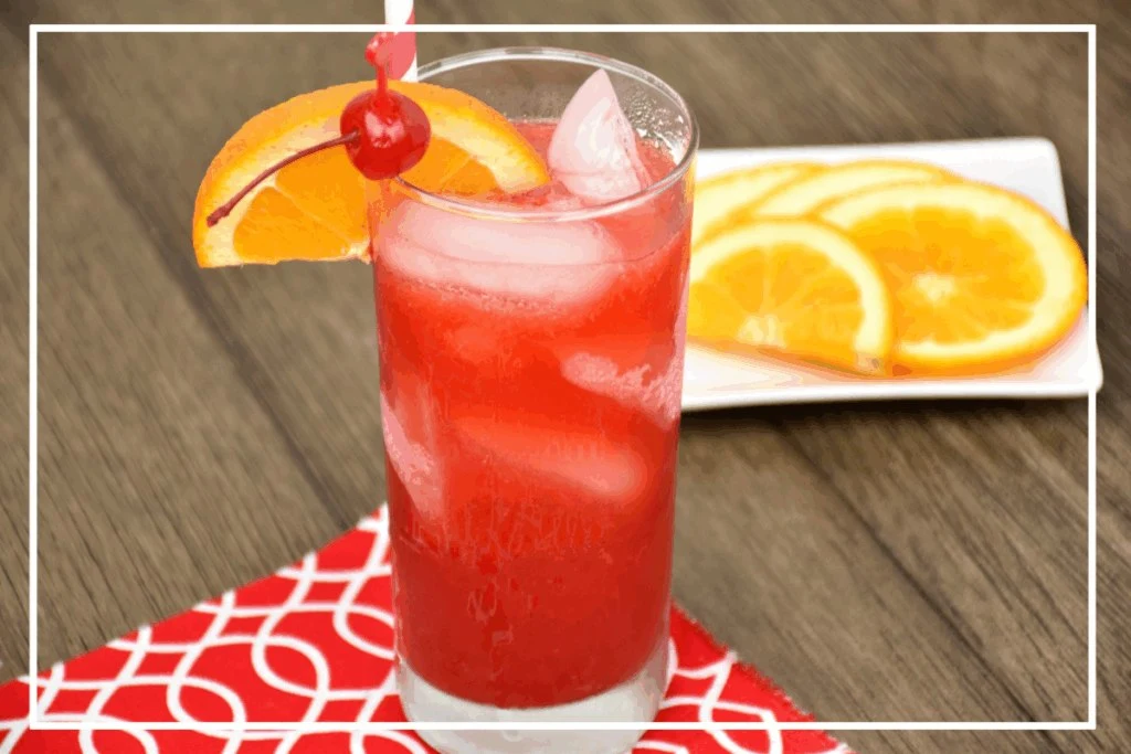 A tall glass filled with an Alabama Slammer cocktail over ice garnished with a slice or orange and a cherry