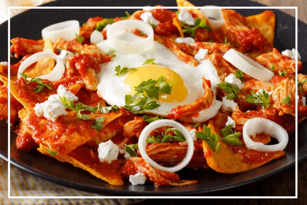 A plate of Chilaquiles Rojos, made of tortillas swimming in red sauce and topped with a fried egg, onion and parsley