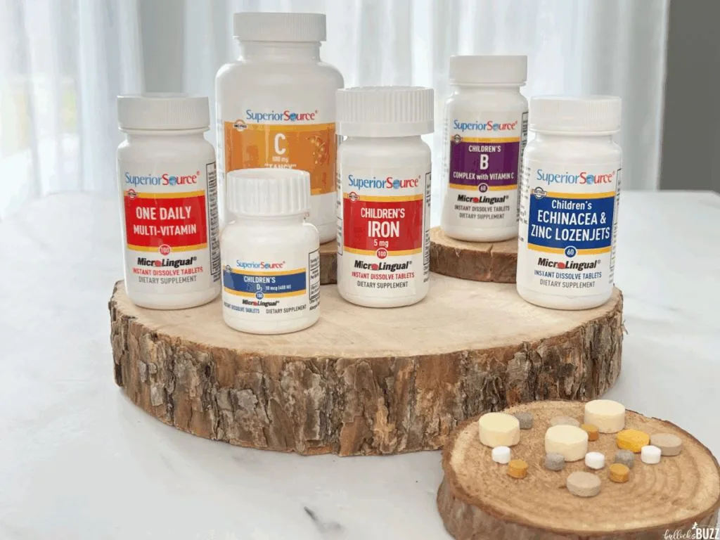 Six bottles of Superior Source Vitamins on a slice of wood in front of some of the vitamins out of the bottles