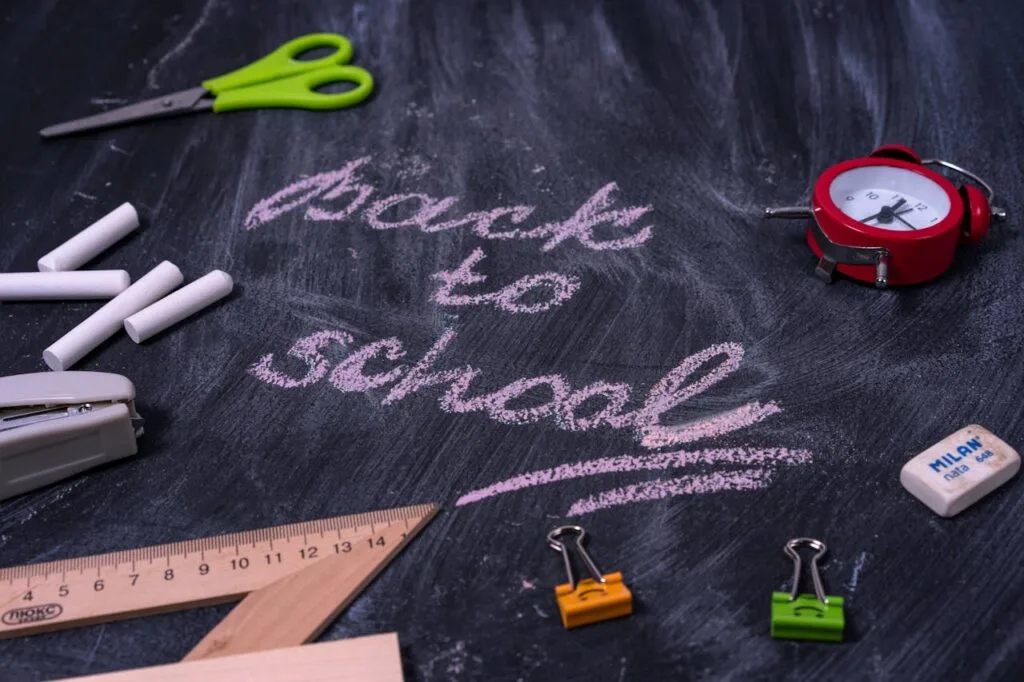 Back-to-school tips for parents illustrated with chalk writing “Back to School” on a blackboard surrounded by school supplies like scissors, chalk, ruler, and alarm clock