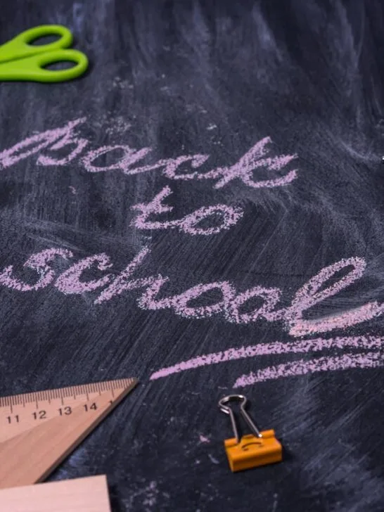 Back-to-school tips for parents illustrated with chalk writing “Back to School” on a blackboard surrounded by school supplies like scissors, chalk, ruler, and alarm clock