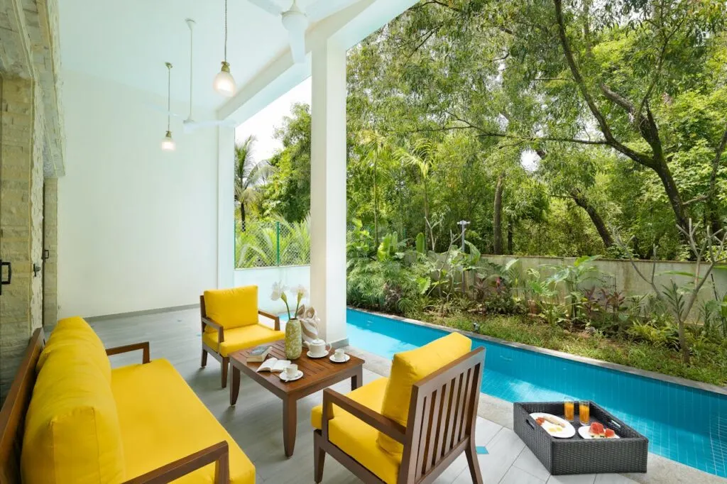 Covered patio with bright yellow furniture beside a pool, an example of practical deck and patio design tips for relaxation and outdoor living.