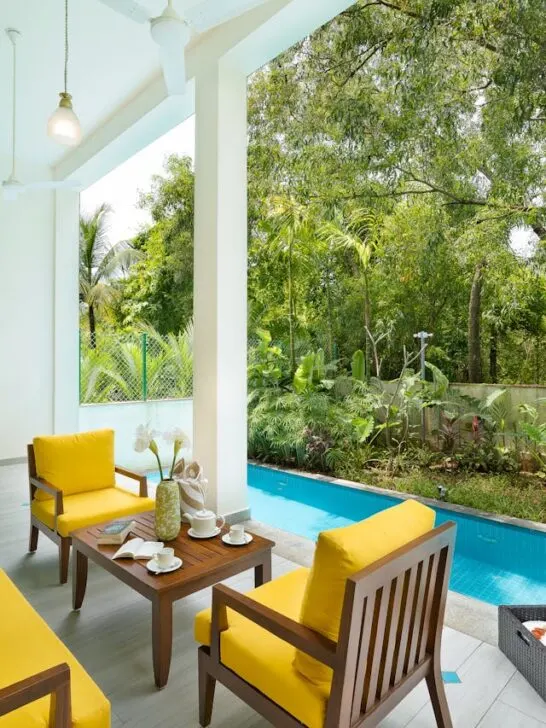 Covered patio with bright yellow furniture beside a pool, an example of practical deck and patio design tips for relaxation and outdoor living.