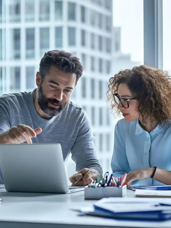 Man explaining something to a woman while reviewing a laptop, illustrating feedback strategies for small business owners in a collaborative setting.
