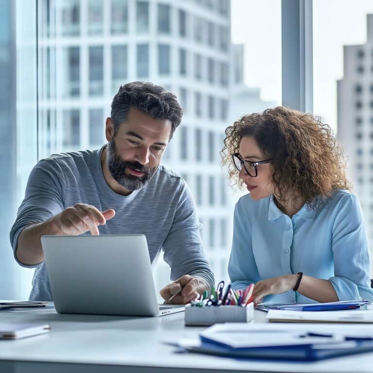 Man explaining something to a woman while reviewing a laptop, illustrating feedback strategies for small business owners in a collaborative setting.