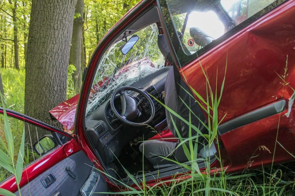 A totaled red car with its door open after crashing into a tree