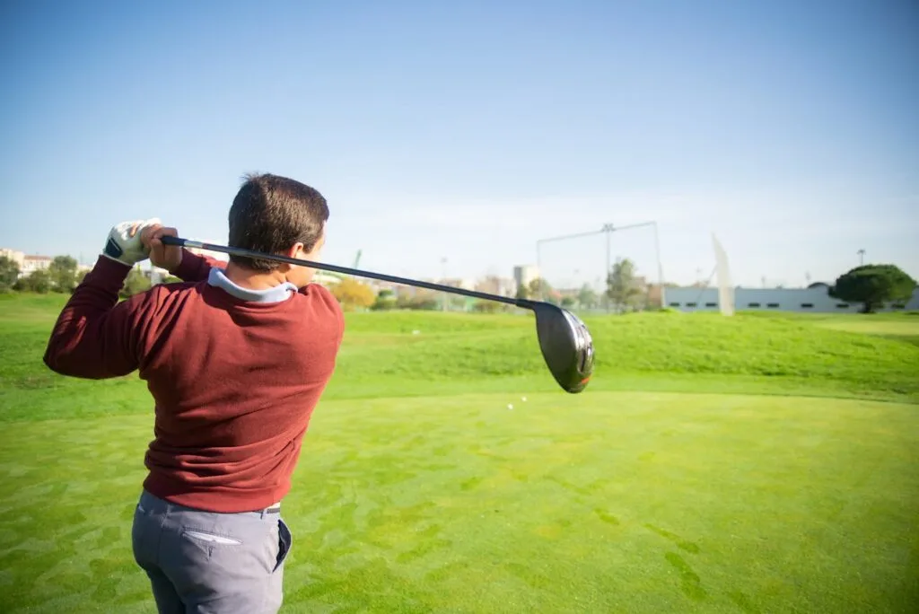 A man mid-swing wearing the proper golf course attire