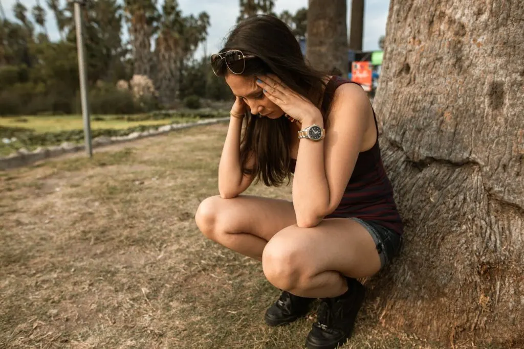 Woman holding her head in stress while sitting outdoors, showing the struggle of how to manage stress and anxiety.