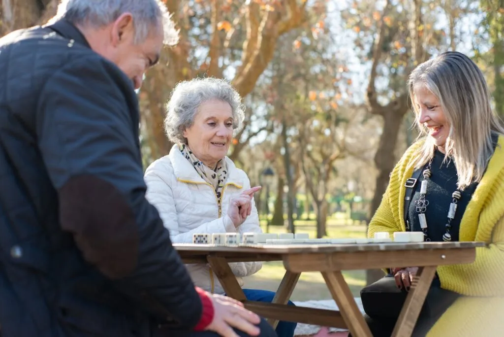 Group of seniors enjoying outdoor activities for seniors by playing a game together at a picnic table in the park