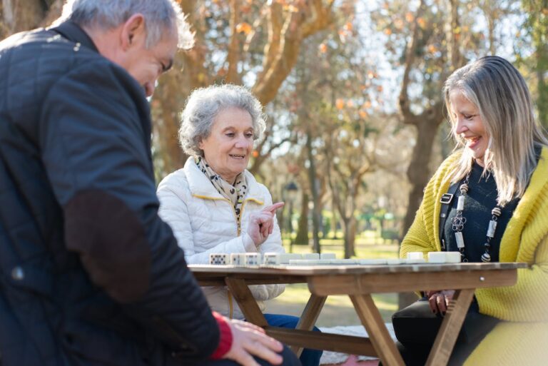 Group of seniors enjoying outdoor activities for seniors by playing a game together at a picnic table in the park